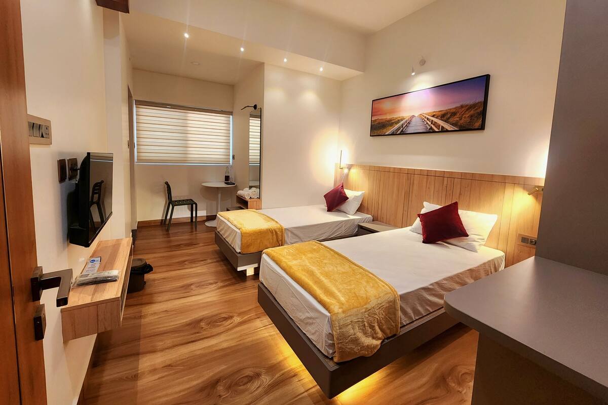 A hotel room with two beds, a TV, a desk, a chair, and a painting on the wall.