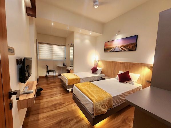 Hotellihuone, jossa on kaksi sänkyä, televisio, työpöytä, tuoli ja taulu seinällä.
