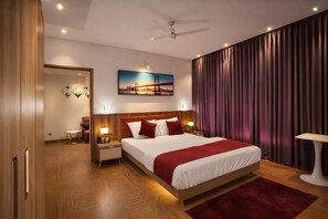Ein Hotelzimmer mit einem großen Bett, Holzböden, einem Deckenventilator, einem Gemälde einer Brücke und Blick auf eine Stadtlandschaft.