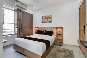 A modern hotel room with a large bed, a wooden wardrobe, a painting on the wall, and a small desk with a lamp. - POP 84260d Hotel City Centre (Pune)