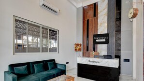 Ein Empfangsschalter mit der Aufschrift 'TOUMHOUSE' und einem Schild mit der Bezeichnung 'Empfang', ein grünes Sofa und ein Holztisch.