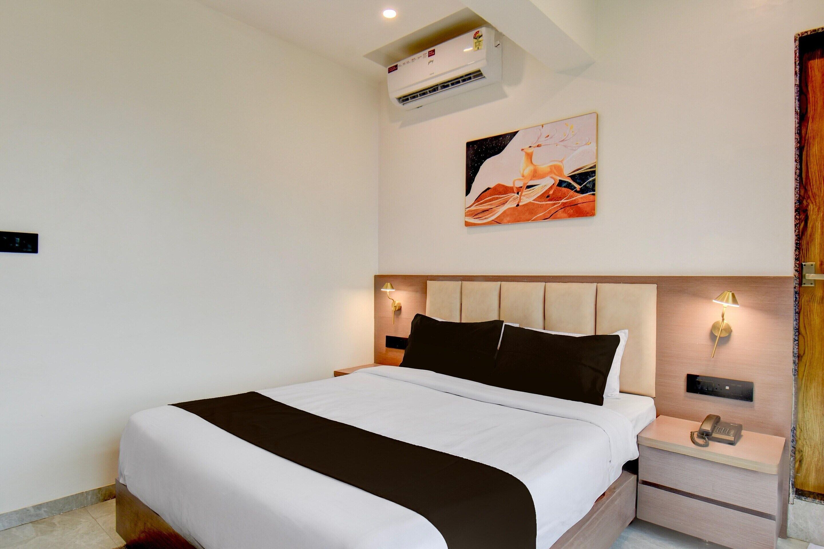 A hotel room with a bed, bedside tables, a wall-mounted phone, an air conditioner, and a painting.