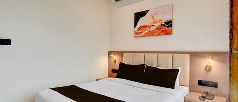 A hotel room with a bed, bedside tables, a wall-mounted phone, an air conditioner, and a painting.