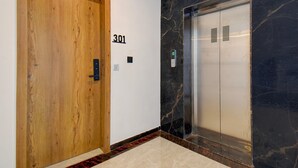 Eine Holztür mit der Nummer 301 an der Wand, ein Aufzug mit Marmorwand und ein rotteppichausgelegter Boden.