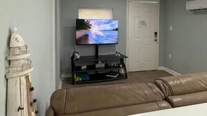 Sala de estar com televisão na parede, sofá de couro marrom e aparador branco com objetos decorativos.