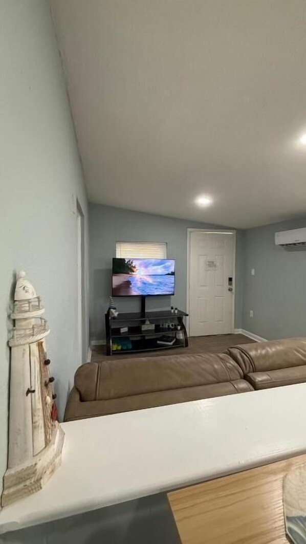 Una sala de estar con un televisor montado en la pared, un sofá de cuero marrón y un mueble blanco con adornos.
