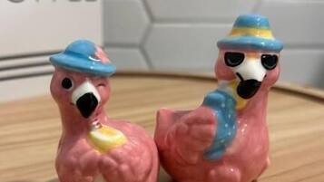 Two pink flamingo figurines on a wooden surface with a hexagonal tile wall in the background.