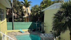Piscina com cerca branca, cercada por palmeiras e uma cerca verde.