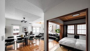 A modern hotel room with a wooden floor, a sofa, a bed, and a dining area with a table and chairs.