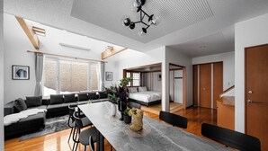 A modern living room with a large dining table, a sofa set, and a kitchen area.