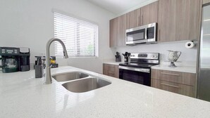 A modern kitchen with stainless steel appliances, a double sink, and wooden cabinets. - Serenity Retreat Wellness Club Yoga Cold Plunge (Florida City)