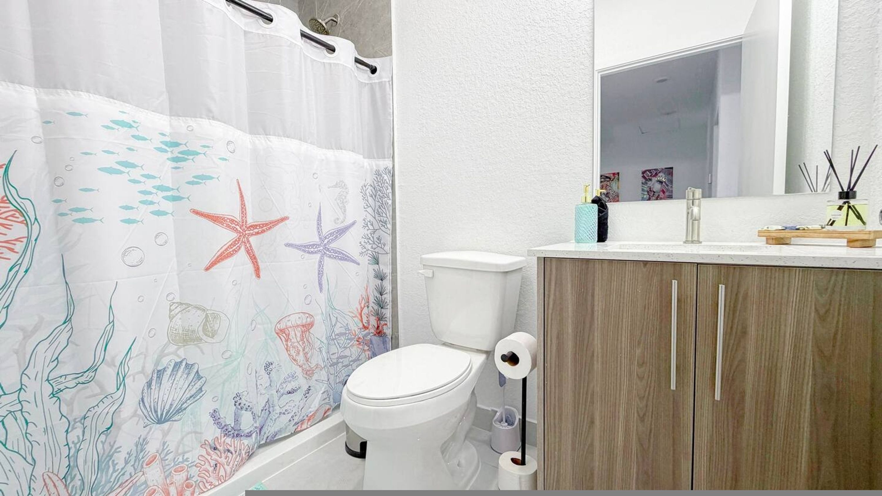 Een badkamer met een wit toilet, houten kastjes, een witte wastafel met spiegel, en een douchegordijn met een maritiem thema.