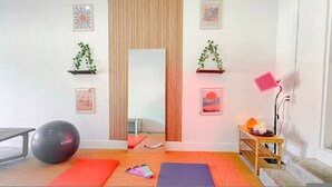 A room with a large mirror, exercise mats, a stationary bike, and a small wooden table with a lamp and candles. - Serenity Retreat Wellness Club Yoga Cold Plunge (Florida City)