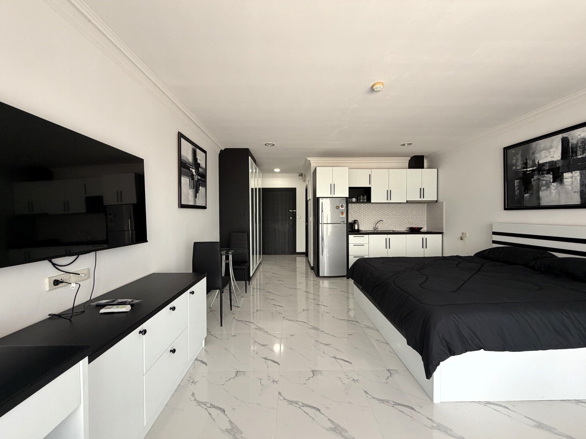A modern bedroom with a large bed, a desk, and a kitchenette.