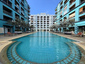 Une piscine dont le bord est recouvert de carreaux, entourée d’un bâtiment doté de nombreux balcons, sous un ciel dégagé.