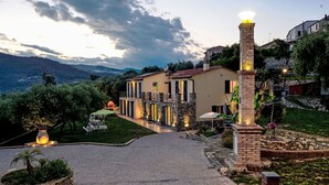 Eine Villa mit einem gepflasterten Weg zum Eingang, umgeben von üppiger Vegetation und Blick auf ferne Berge.