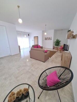 Un salon moderne avec un canapé, un fauteuil noir et une table en verre, où un chien duveteux se prélasse.