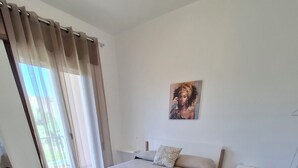 Een slaapkamer met een bed, een schilderij aan de muur, een stoel en een raam met gordijnen.