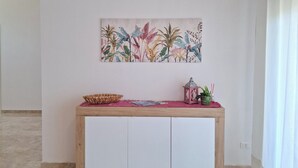 Een kamer met een houten console tafel, kleurrijke planten decoratie aan de muur, een kleine potplant en een rieten mand.