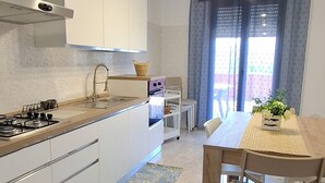 Een moderne keuken met witte kastjes, een gasfornuis, en een eethoek met een houten tafel en stoelen.