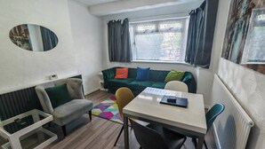 Un espacio habitable compacto con sofá, una mesita, una silla, un espejo y una ventana con cortinas.