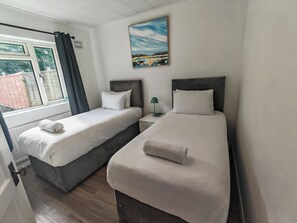 A hotel room with two beds, a window with curtains, a painting on the wall, and a bedside table with a lamp. - Apartment With Private entrance, parking & Garden, few minutes to Town Centre (Borehamwood)