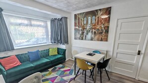Una sala de estar moderna con un sofá verde, un sillón blanco, una mesa de comedor con sillas y una alfombra colorida.