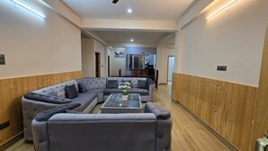 A modern living room with a sectional sofa, a glass coffee table, wooden paneling, and recessed lighting. - Aashvika Homes (Manali)