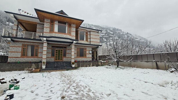 A two-story house with a balcony, a stone facade, and a snowy landscape in the background. - Aashvika Homes (Manali)