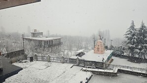 A snowy landscape with a building featuring a bell tower, surrounded by snow-covered trees and a fence. - Aashvika Homes (Manali)