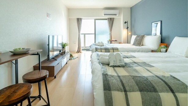 A hotel room with a bed, a desk with a chair, a small table, and a window with curtains. - Chuan House Imazato (Osaka)