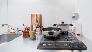 A modern kitchen with a gas stove, two pots, a coffee maker, and a sink. - Chuan House Imazato (Osaka)