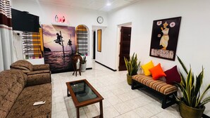 A living room with a sofa, a coffee table, a TV, a mural, and a plant. - Nishi Villa (Negombo)