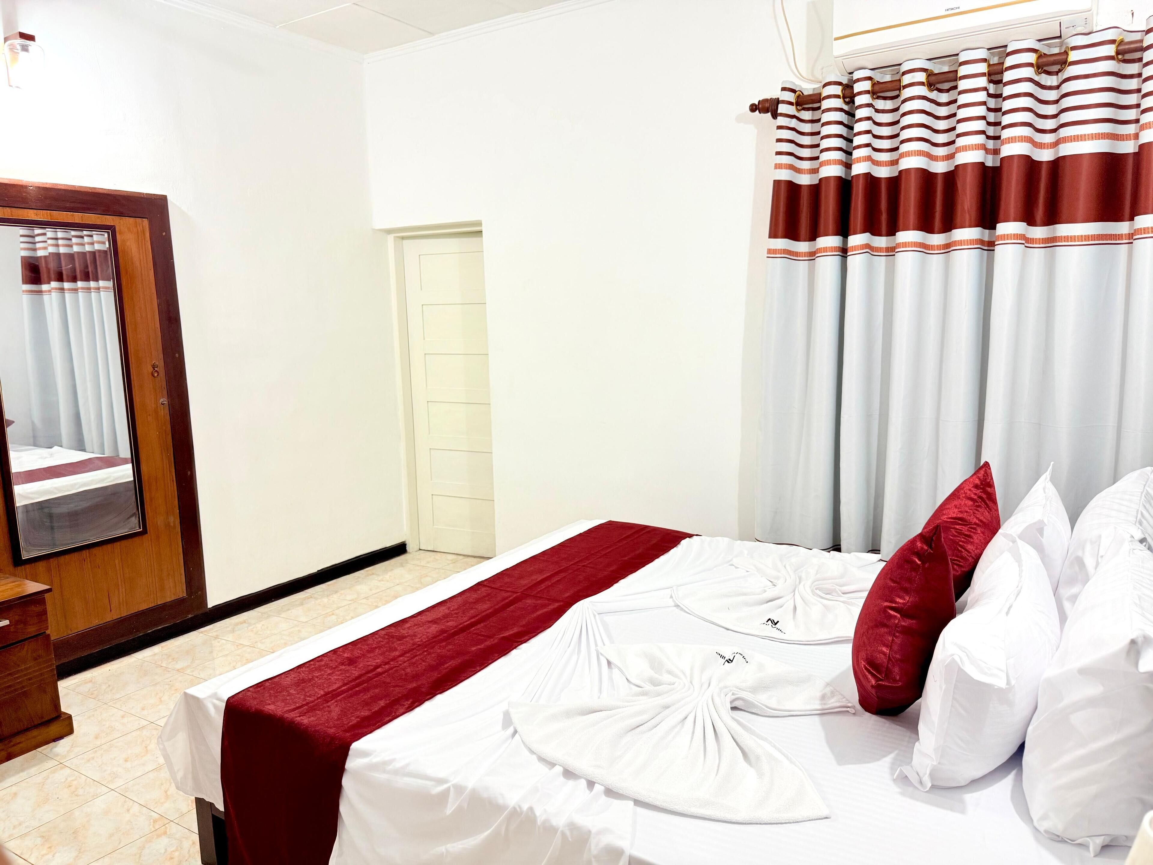 A hotel room with a bed, a wooden wardrobe, a mirror, a door, and curtains.