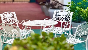 A white metal outdoor seating area with a round table and chairs, surrounded by potted plants. - Nishi Villa (Negombo)