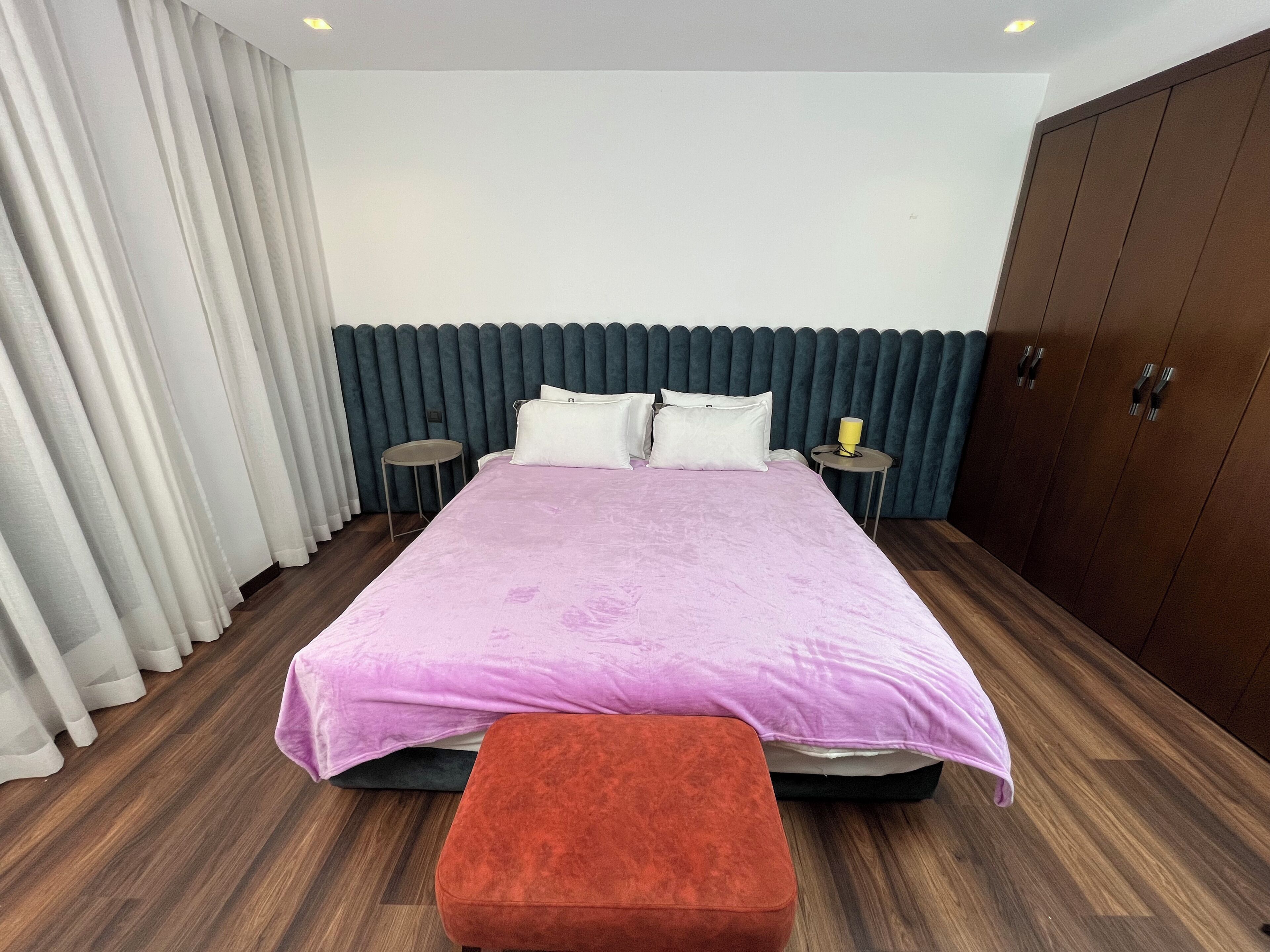 A bedroom with a bed, two bedside tables, a nightstand, a wardrobe, and a window with curtains.