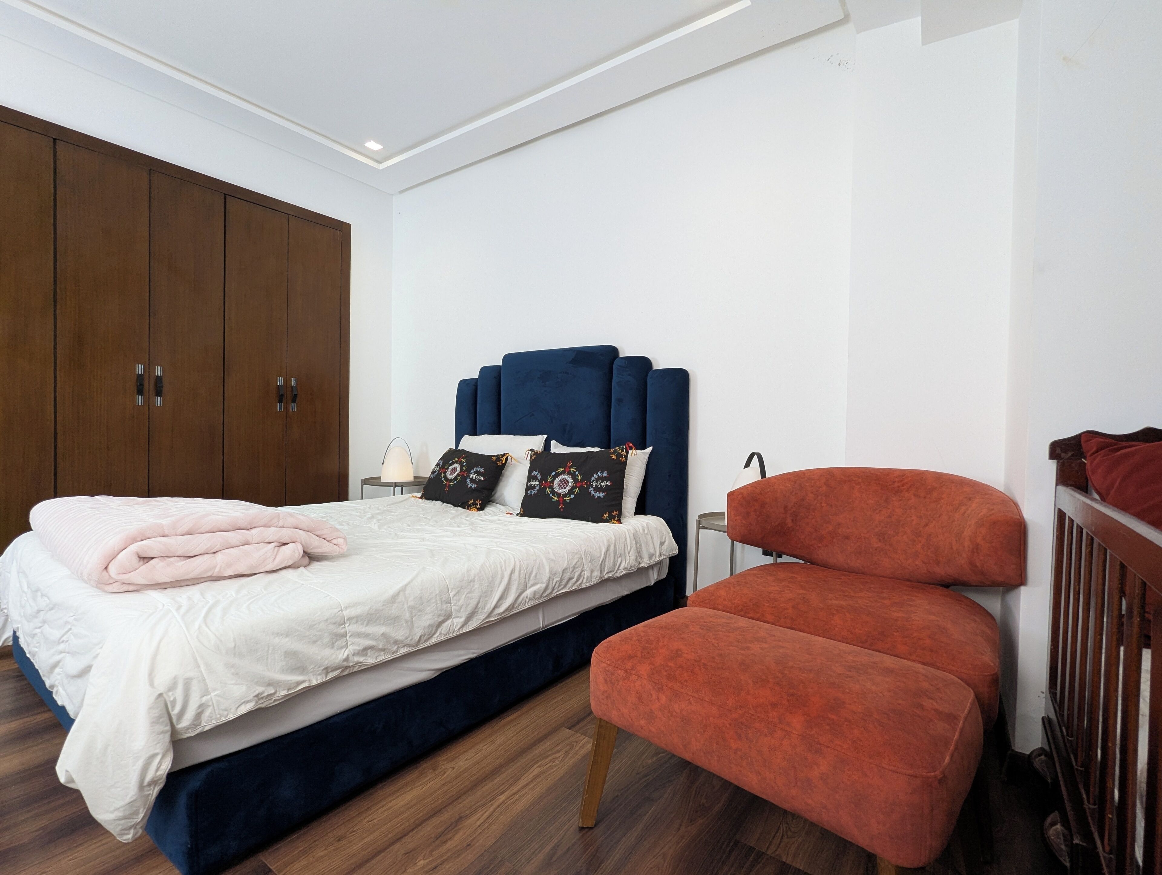 A bedroom with a bed, a wardrobe, a nightstand, and a red chair.