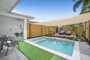 A modern outdoor pool area with a wooden deck, lounge chairs, and a glass table. - Belle Escapes Life's A Beach with Heated Pool (Clifton Beach)