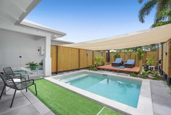 Un área de piscina moderna al aire libre con cubierta de madera, sillas de descanso y una mesa de vidrio.