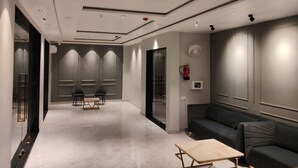 A modern hotel lobby with a marble floor, a sofa, a small table, and a fire extinguisher on the wall. - Nandvilas Hotel (Chunar)