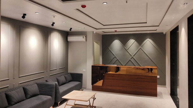 A modern reception area with a wooden reception desk, grey upholstered sofas, and recessed lighting. - Nandvilas Hotel (Chunar)
