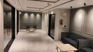 A modern hotel lobby with a marble floor, two dark sofas, a wooden coffee table, and a glass partition with a metal railing. - Nandvilas Hotel (Chunar)