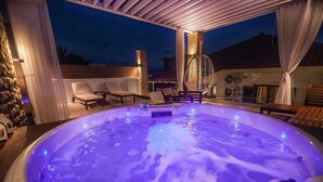 Un jacuzzi con maderas y sillas reclinables, rodeado por un porche cubierto con cortinas.