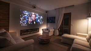 Una sala de estar moderna con chimenea, asientos cómodos y una pantalla grande para ver películas.