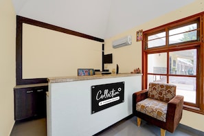 Un área de recepción con un cartel que dice 'Collection', una ventana con marco de madera y un sillón estampado.