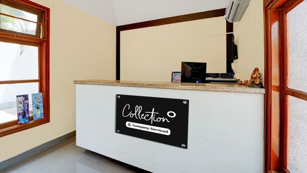 A reception desk with a sign reading 'Collection Company-Serviced,' a window with artwork, and a small statue on the counter. - Classic Hotel Phoenix (Valappadi)