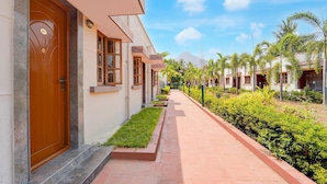 A hotel corridor with a wooden door marked '021', a paved walkway, and a row of palm trees. - Classic Hotel Phoenix (Valappadi)