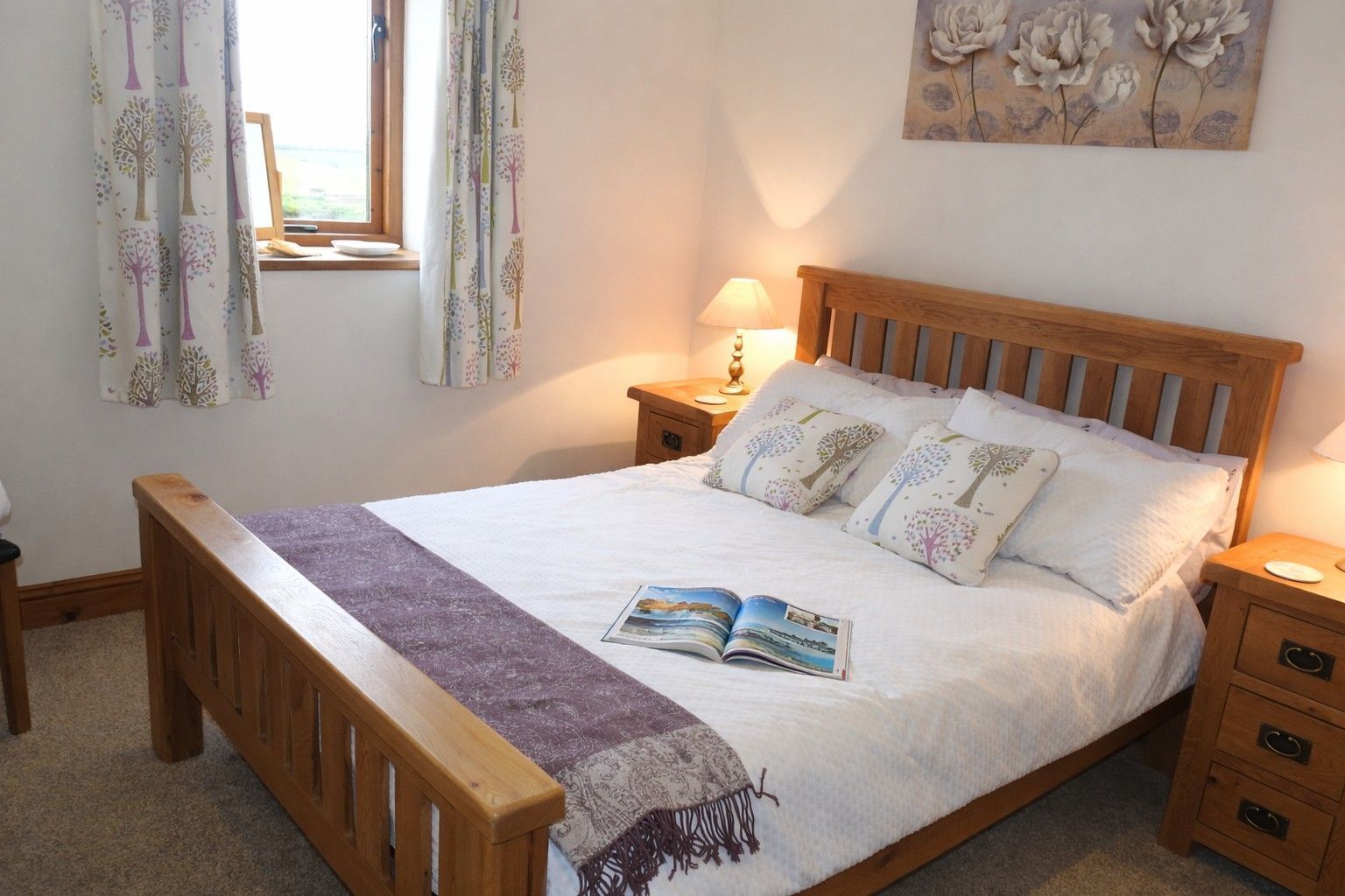 Une chambre à coucher avec un lit en bois, une table de chevet avec une lampe, une fenêtre avec des rideaux et un tableau accroché au mur.