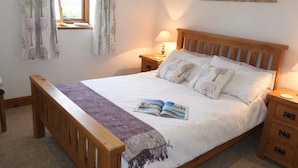 Une chambre à coucher avec un lit en bois, une table de chevet avec une lampe, une fenêtre avec des rideaux et un tableau accroché au mur.