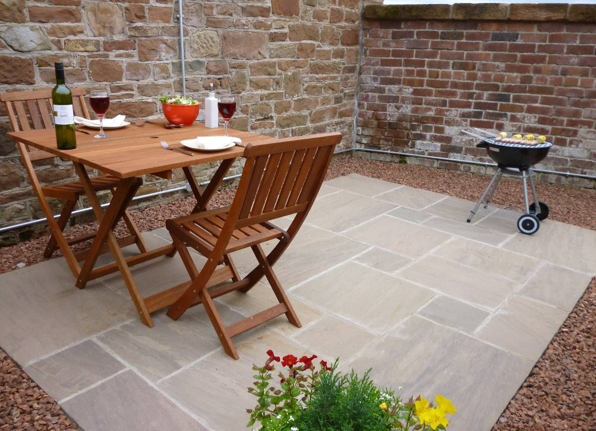 Un conjunto de mesa y sillas de madera en un patio con un muro de piedra y un muro de ladrillo al fondo.